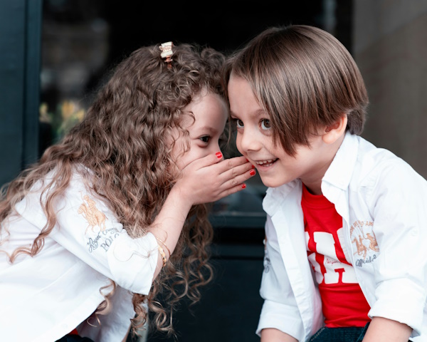 Little girl whispering to a little boy