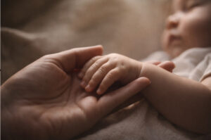 An adult hand holding a hand of an infant