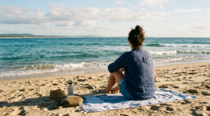a woman on the beach looking at the sea while sitting on the sand