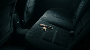 A lonely keychain resting on the dark, plush back seat of a car, illuminated by a single, soft shaft of light.